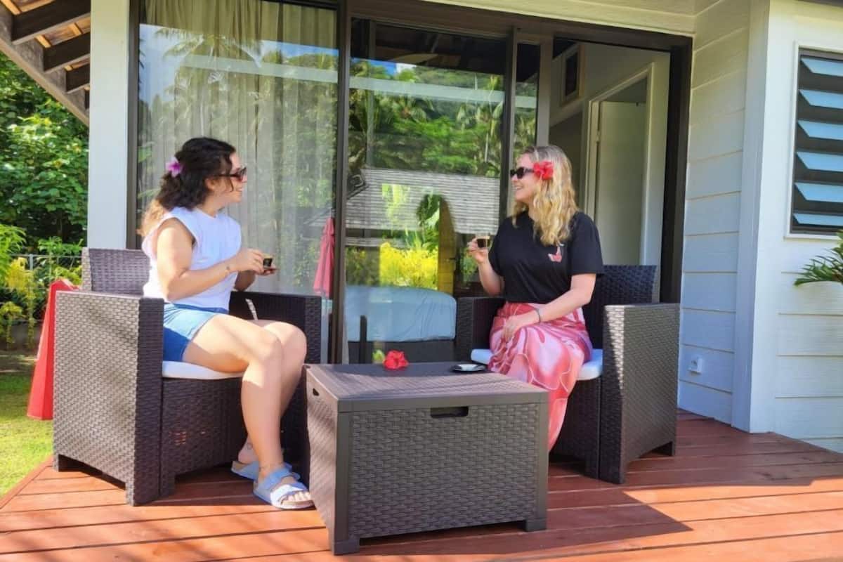 Two people seated on wicker chairs on an outdoor deck with a glass door leading to a garden.