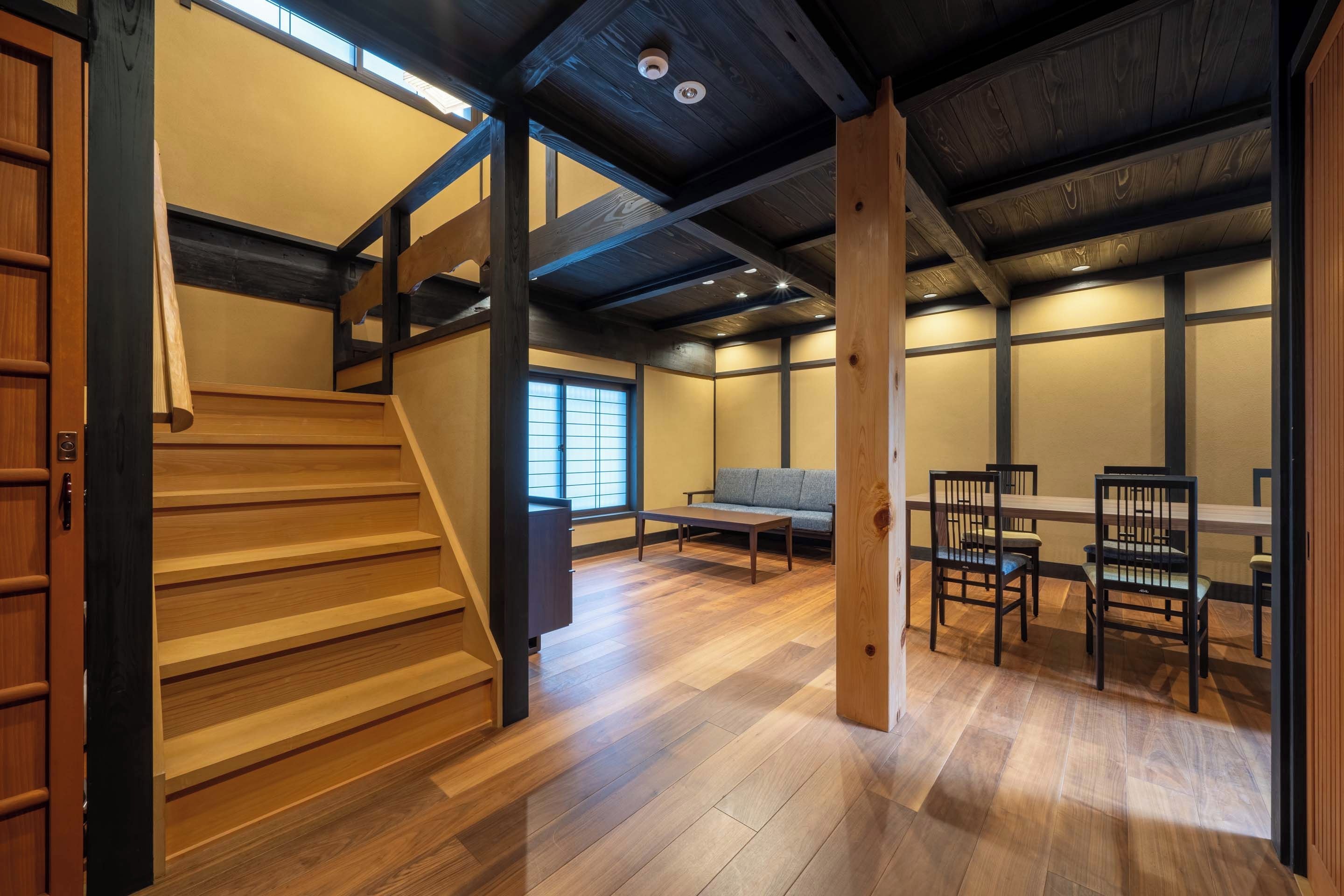 A traditional Japanese-style room with a wooden staircase, tatami mat flooring, a low table, and a sofa.