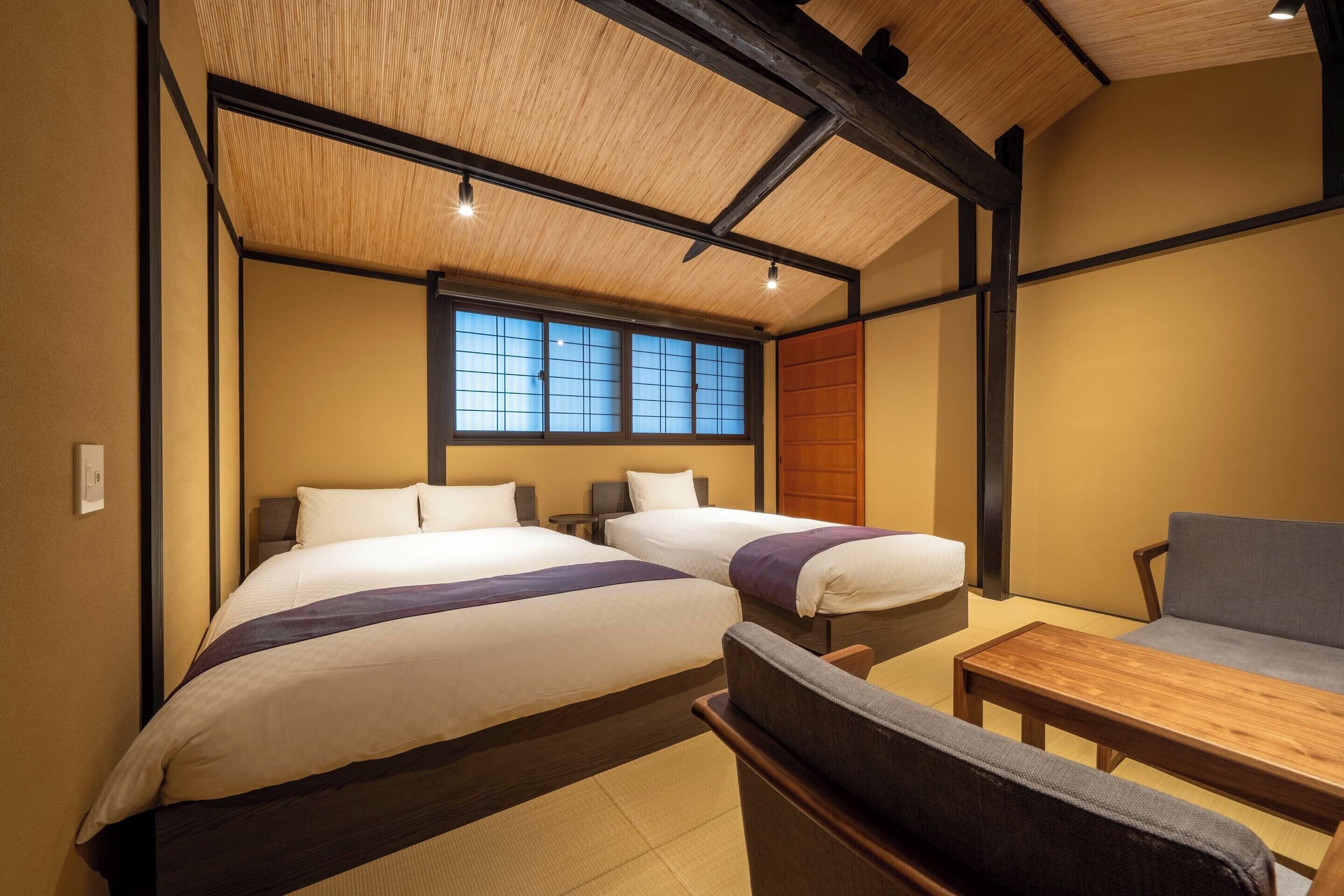 A hotel room with two beds, a wooden ceiling, a window, and a sofa.