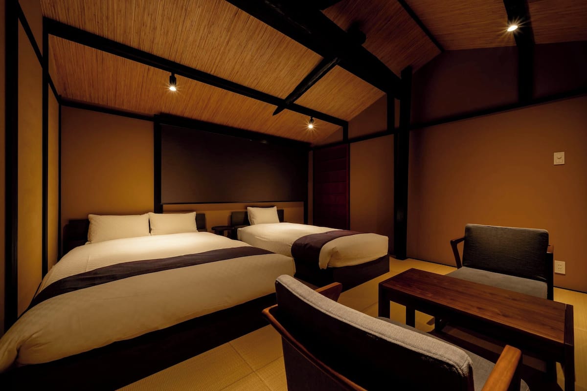 A hotel room with two beds, a wooden table, and a chair.