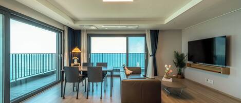 Una habitación de hotel moderna con una cama grande, un sofá, un comedor, un televisor y un balcón con vistas.
