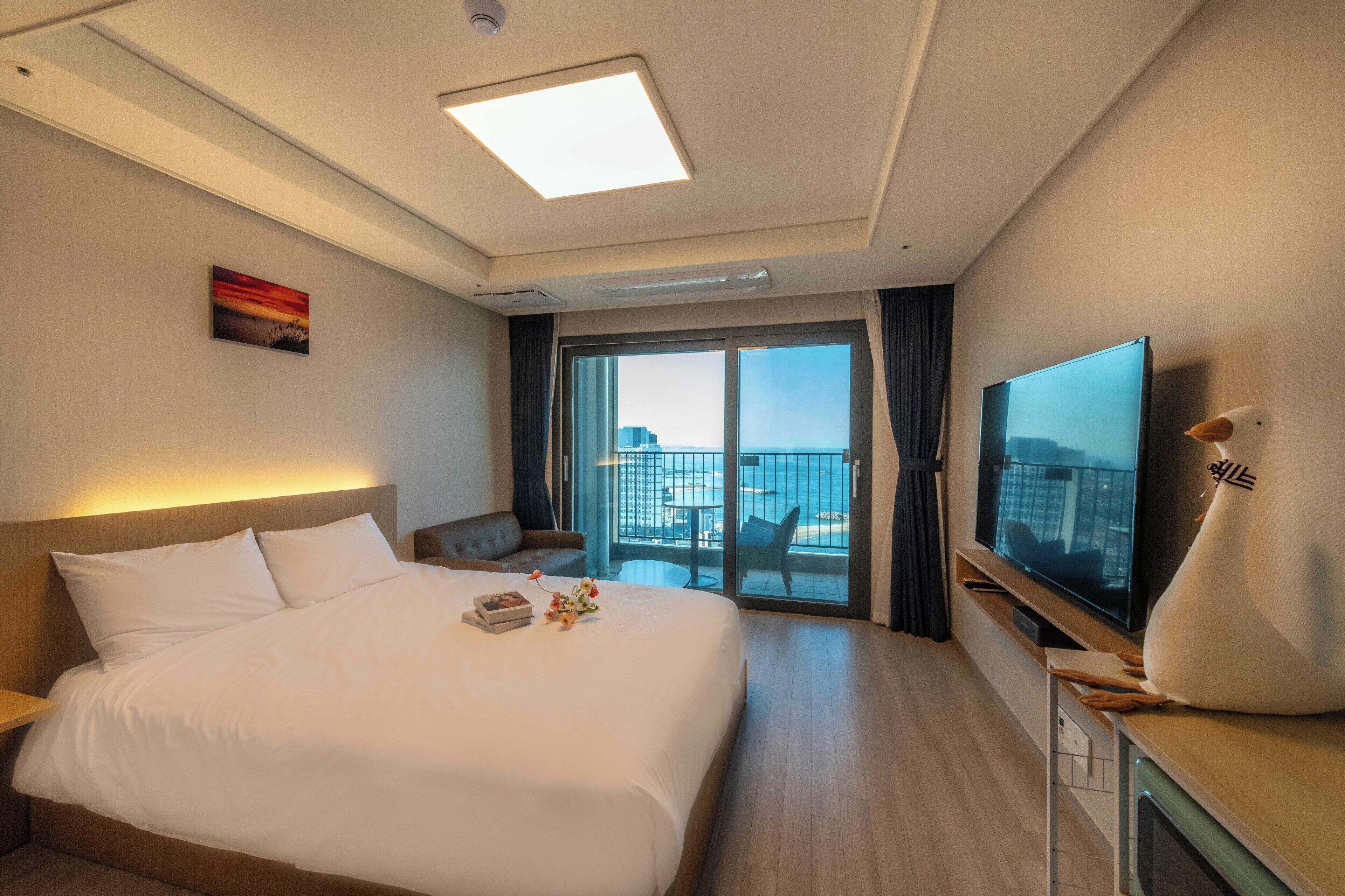Habitación de hotel con cama, televisor de pantalla plana, balcón con vistas e iluminación en el techo.
