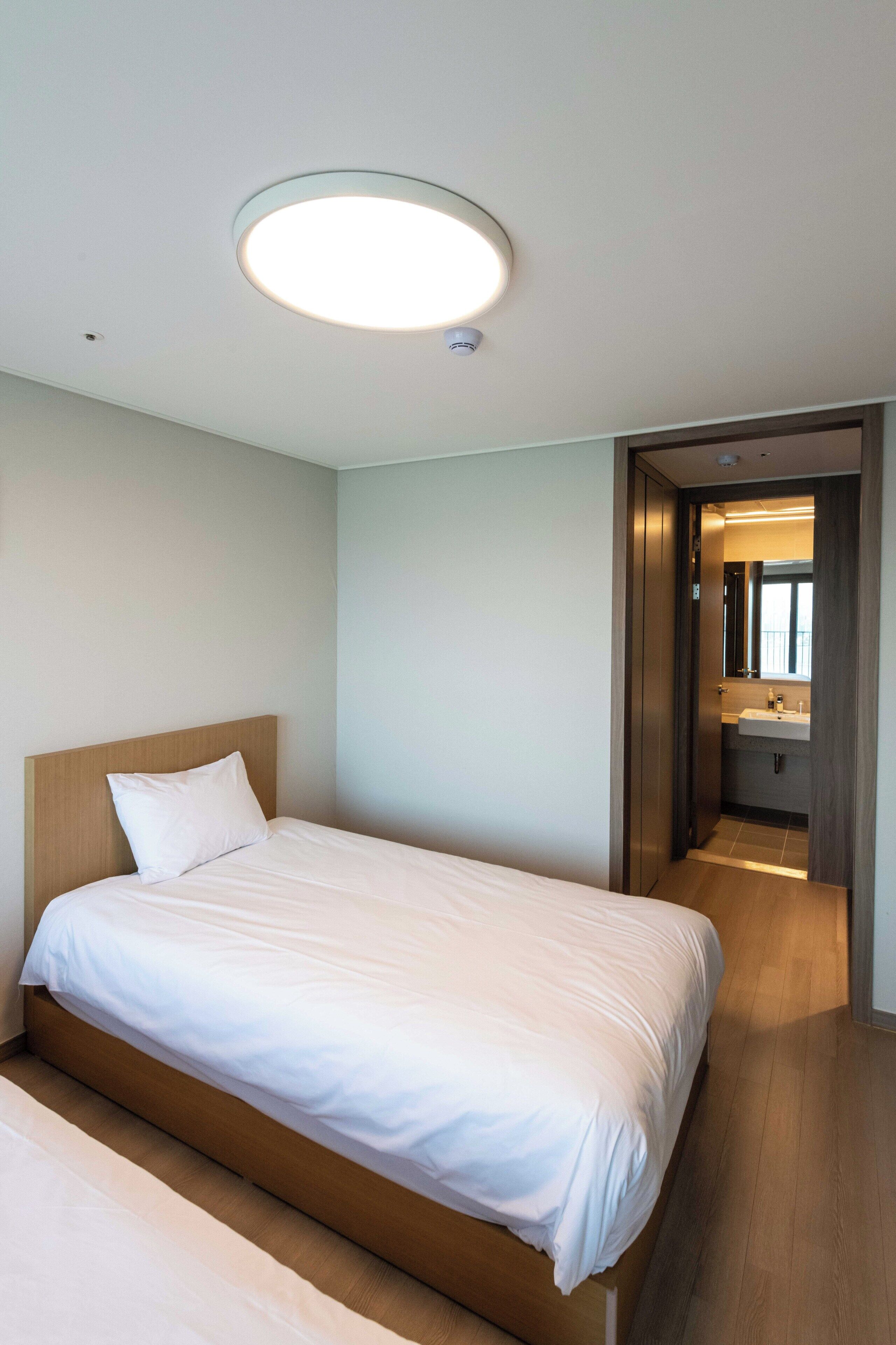 Una camera d'hotel moderna con un letto grande, una lampada a soffitto rotonda e vista sul bagno.