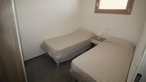Allotjament petit, d'una sola habitació, amb dos llits individuals, una tauleta de nit i una finestra.