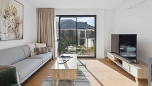 A modern living room with a sofa, coffee table, TV, and a sliding glass door leading to a balcony.