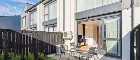 A modern two-story house with a patio area featuring a table and chairs, an air conditioning unit, and a black fence.