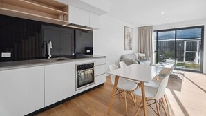 A modern kitchen with white cabinetry, a built-in oven, and a dining area with a white table and chairs.