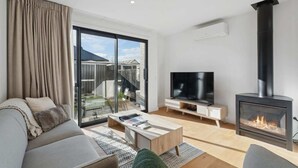 A modern living room with a sofa, TV, fireplace, and a sliding glass door leading to a balcony.