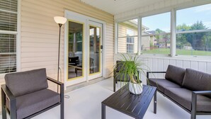 Een overdekt terras met een bank, stoelen en een tafel.