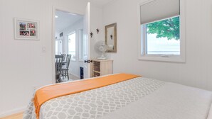 A bedroom with a bed, a window with a view, a fan, and a door leading to another room. - Lakefront Escape on Beautiful Burt Lake! (Alanson)