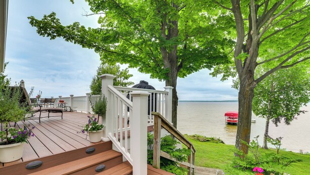 A wooden deck with a white railing, potted plants, and a view of a lake. - Lakefront Escape on Beautiful Burt Lake! (Alanson)