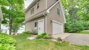 A two-story house with a garage, surrounded by a well-maintained lawn and various plants. - Lakefront Escape on Beautiful Burt Lake! (Alanson)