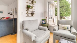 A cozy living room with two grey armchairs, a coffee table, a bookshelf, and a window with a view of trees. - Lakefront Escape on Beautiful Burt Lake! (Alanson)