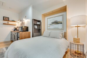 Une chambre à coucher avec un grand lit, une table de chevet en bois, une lampe, une étagère avec des objets décoratifs et un tableau au mur.