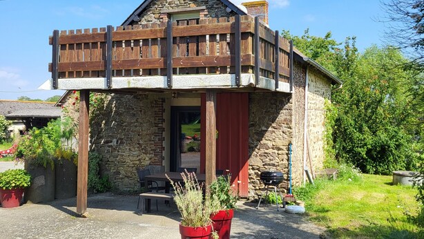 A rustic stone building with a wooden balcony, surrounded by greenery and potted plants. - Charming 2-bedroom house in soothing Cuillé with WiFi (Cuillé)