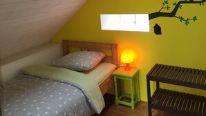 A small, cozy bedroom with a sloped ceiling, a skylight, a bed with a polka dot bedspread, a nightstand with a lamp, and a wall mural of a tree. - Charming 2-bedroom house in soothing Cuillé with WiFi (Cuillé)