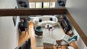 A spacious living area with a white sofa, a green armchair, and a wooden coffee table. A dining table with chairs is visible in the background.