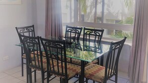 A dining area with a glass-top table and black chairs with patterned cushions. - U09 Tripcony 2 Bedroom w Balcony (Caloundra)