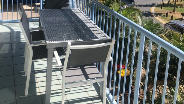A balcony with a table and chairs, overlooking a body of water and a parking area. - U09 Tripcony 2 Bedroom w Balcony (Caloundra)