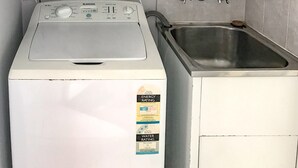 A compact laundry area with a front-loading washer and a sink. - U09 Tripcony 2 Bedroom w Balcony (Caloundra)