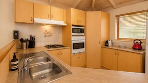 A kitchen with wooden cabinets, a stainless steel sink, a gas stove, an oven, and a window with blinds. - Bird's Nest (Dunsborough)