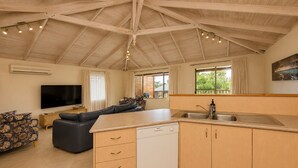 A spacious living area with a sofa, a flat-screen TV, and a kitchen with a dishwasher and sink. - Bird's Nest (Dunsborough)