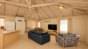 A spacious living area with a high ceiling, a flat-screen TV, a sofa, a patterned armchair, and a kitchen counter. - Bird's Nest (Dunsborough)