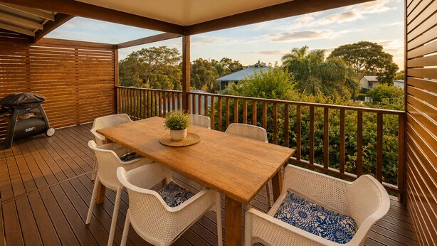 A wooden deck with a table and chairs, a grill, and a view of trees and houses. - Bird's Nest (Dunsborough)