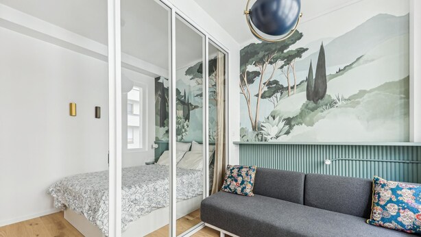 A modern bedroom with a sliding glass door, a gray sofa with patterned cushions, and a large mural of trees on the wall. - Art and comfort near the Bastille (Paris)