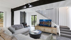 A modern living room with a grey sofa, a black coffee table, a TV on a wooden cabinet, a fireplace, and a staircase. - Waterfront Getaway, Pet Friendly - Jervis Bay - Book 3 Nights, Pay for 2 until 24 September 2026 (Saint Georges Basin)