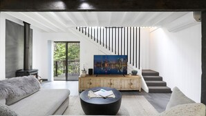 A modern living room with a large flat-screen TV, a sofa, a coffee table, and a staircase leading to an outdoor area. - Waterfront Getaway, Pet Friendly - Jervis Bay - Book 3 Nights, Pay for 2 until 24 September 2026 (Saint Georges Basin)