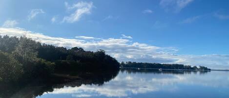 Um lago calmo com margens arborizadas e uma ponte ao longe.