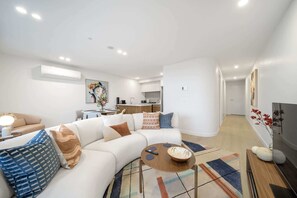 Una sala de estar moderna con un sofá seccional, una mesa de centro y una cocina al fondo.