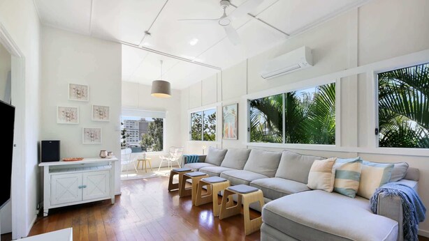 A modern living room with a sectional sofa, wooden coffee table, and a dining area with a white cabinet and chairs. - 2-Bed Beach House in Burleigh Heads Amidst Nature (Burleigh Heads)