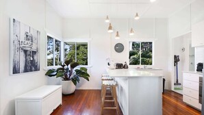 A modern kitchen with a central island, wooden flooring, white cabinetry, and pendant lighting. - 2-Bed Beach House in Burleigh Heads Amidst Nature (Burleigh Heads)