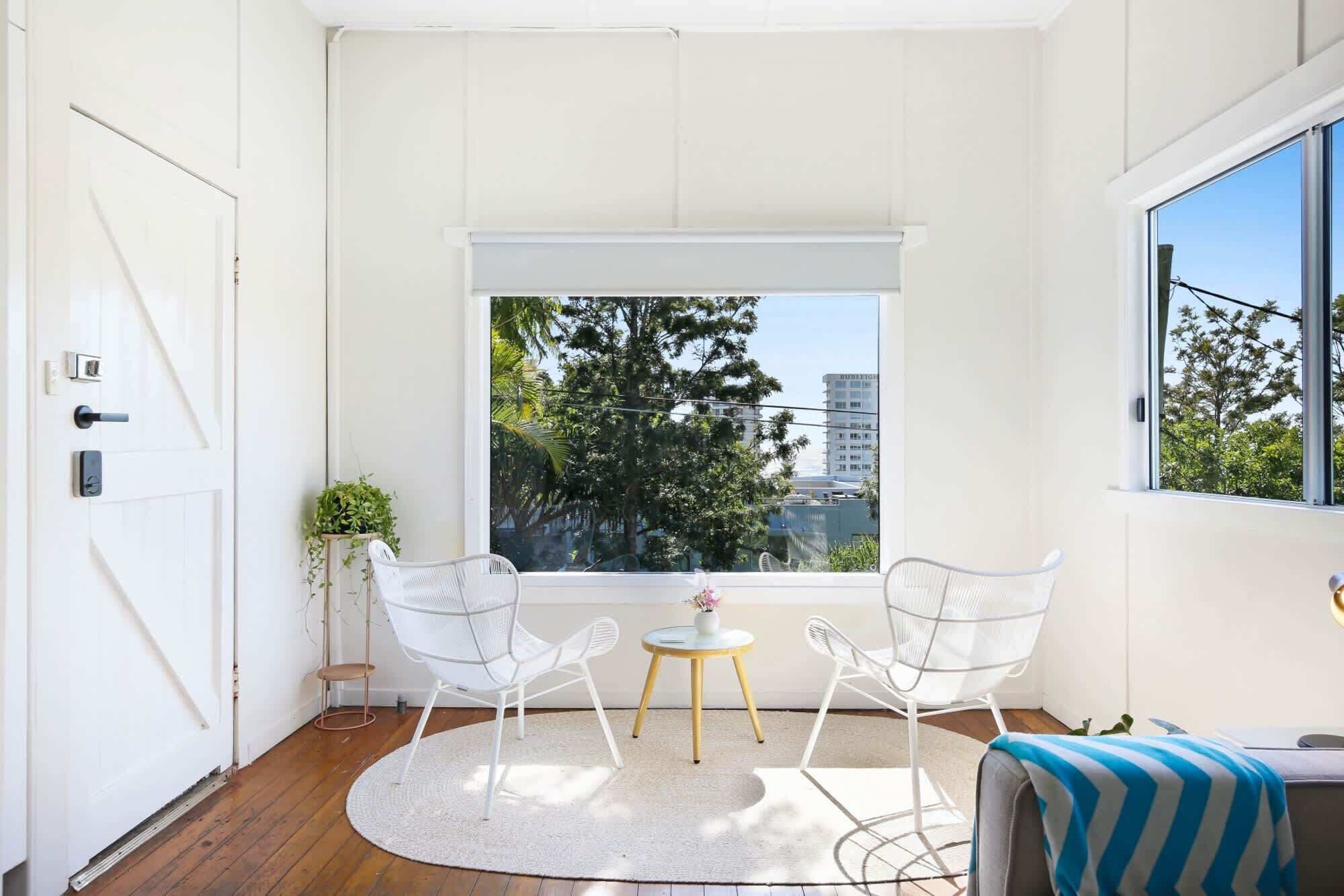 A room with a large window, two white chairs, a small round table, and a blue-striped cushion.