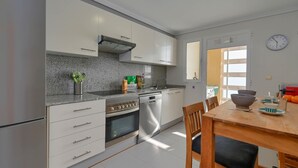Une cuisine moderne avec des armoires blanches, une cuisinière en acier inoxydable et un lave-vaisselle. On y trouve une table à manger en bois avec des chaises.