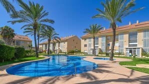 Une piscine entourée de palmiers et un bâtiment doté d’un toit en tuiles.