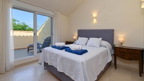 Une chambre dotée d’un grand lit, d’une table de chevet, d’une lampe et d’une porte-fenêtre coulissante donnant sur un espace extérieur.