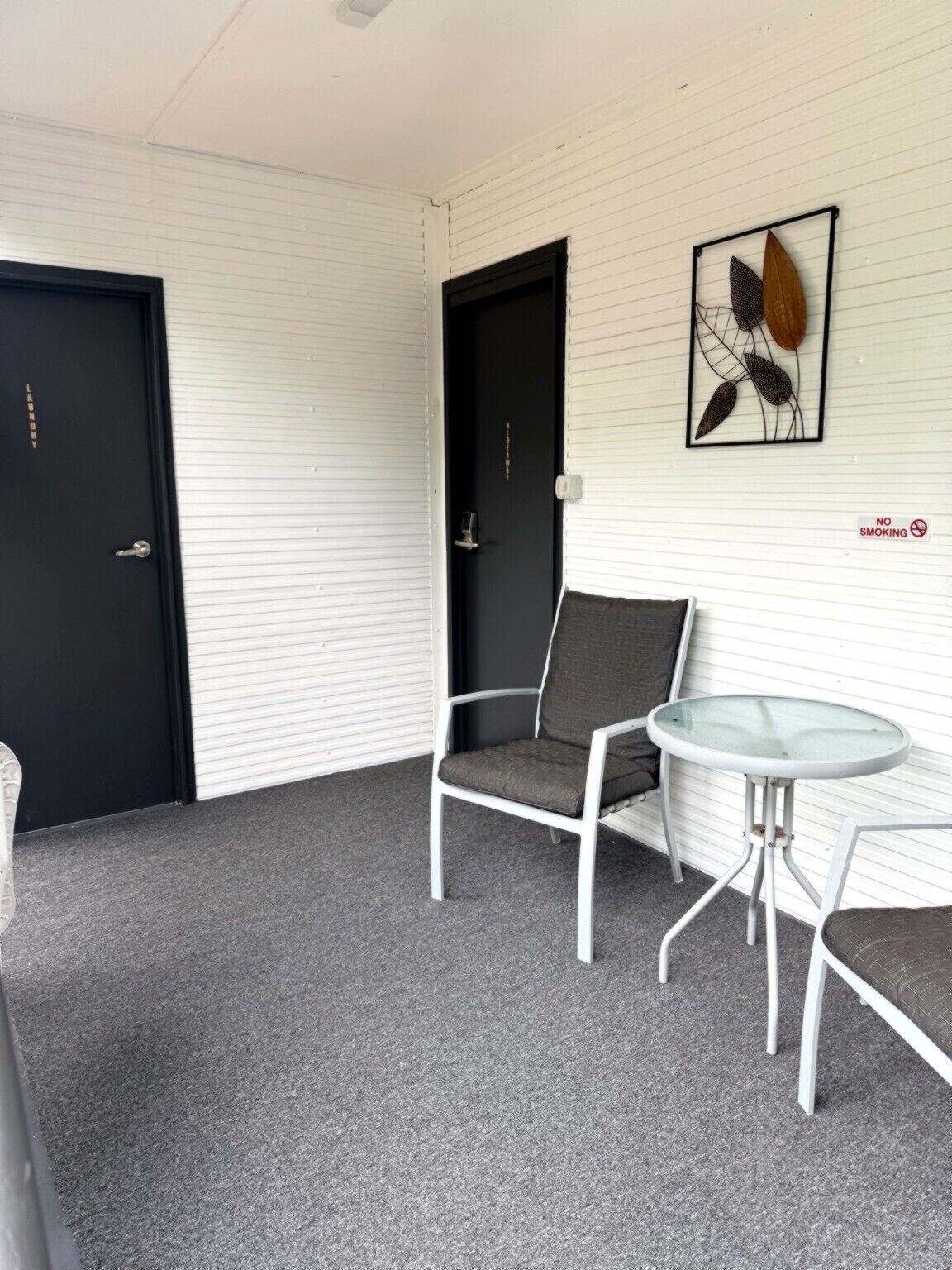 A room with a closed door, a chair, a table, and a wall-mounted artwork.