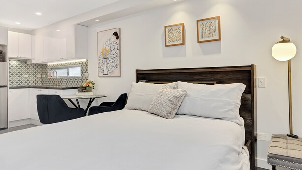 Una habitación de hotel moderna con una cama grande, una mesa de comedor y una kitchenette al fondo.