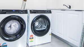Dos lavadoras de carga frontal en un cuarto de lavado con armarios blancos y piso de baldosas.