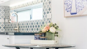 Una cocina con un salpicadero decorado, una ventana y una mesa con un florero y frascos.