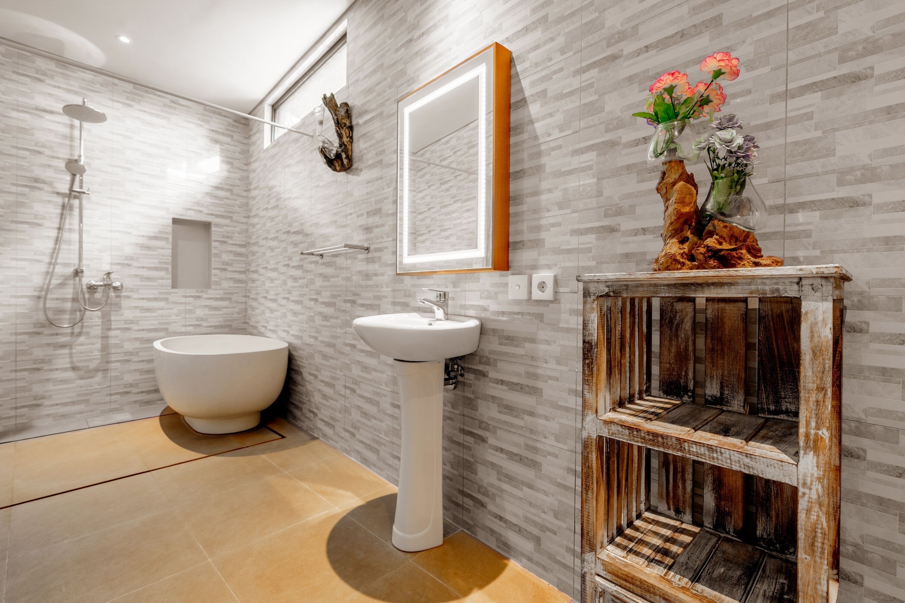 A modern bathroom with a freestanding bathtub, a pedestal sink, and a vanity with a rustic wooden shelf.