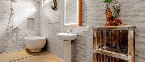 A modern bathroom with a freestanding bathtub, a pedestal sink, and a vanity with a rustic wooden shelf.