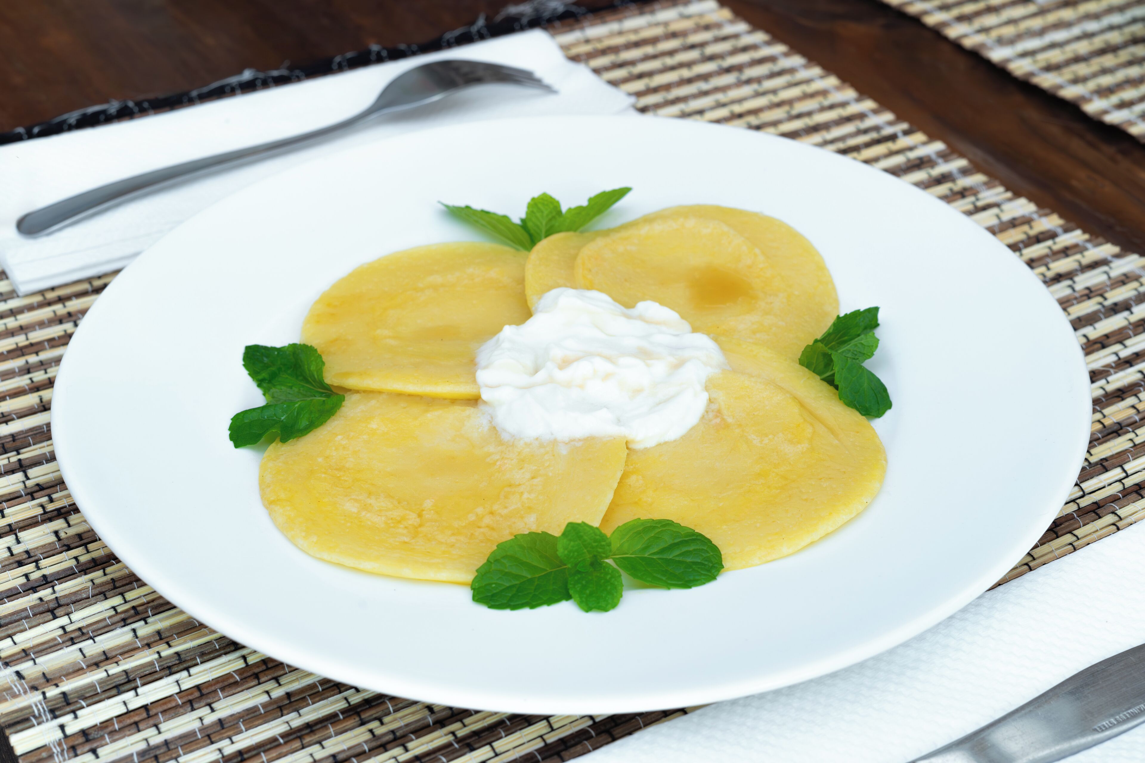 Un plato de crepes con crema batida y hojas de menta sobre un plato blanco.