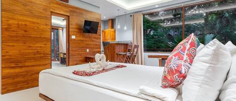 A modern hotel room with a wooden accent wall, a large bed with white linens, a TV mounted on the wall, and a view of lush greenery through the window.