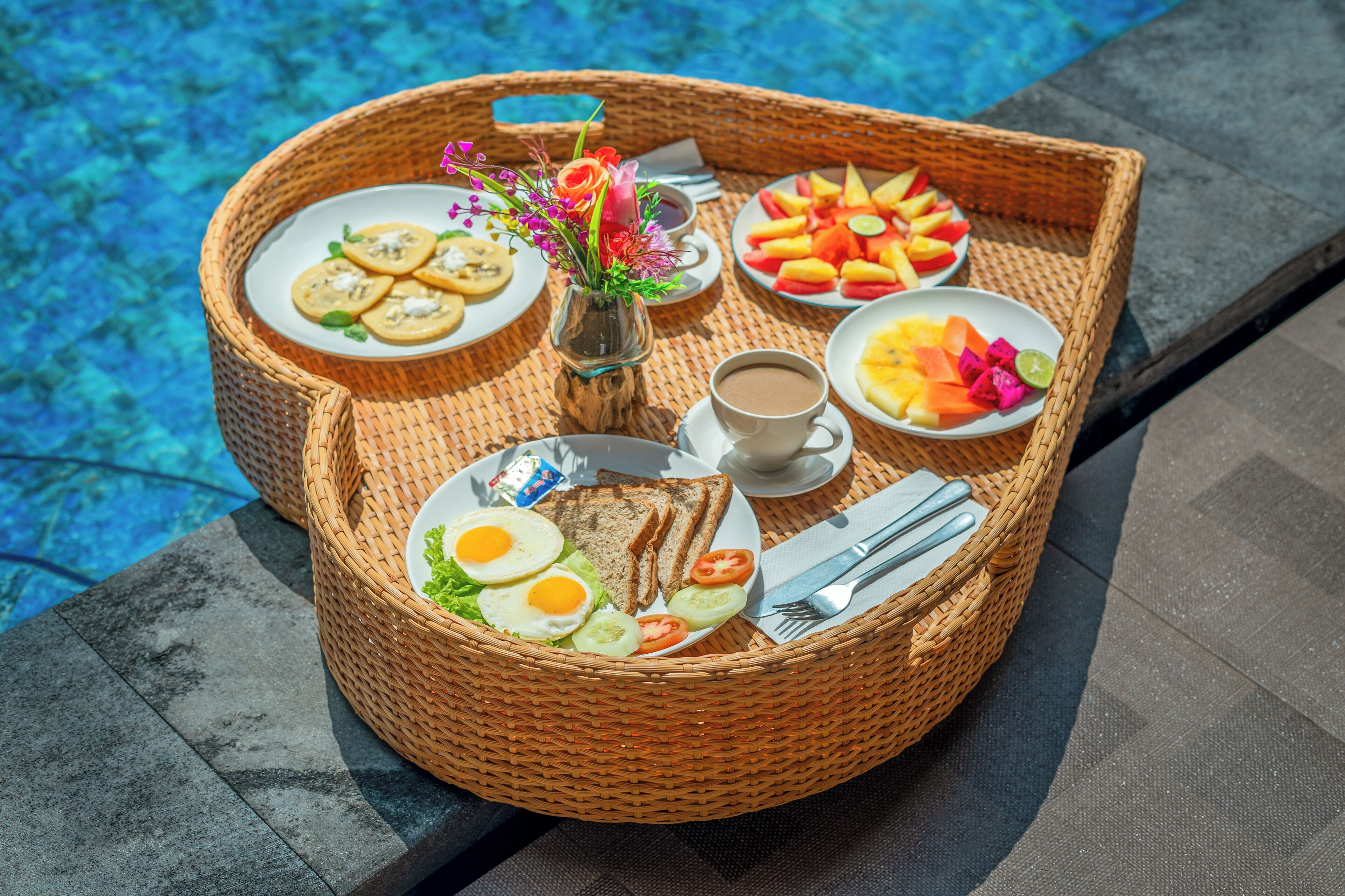 A breakfast tray with eggs, toast, fruit, and coffee by a pool.