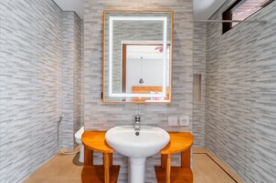 Un baño moderno con lavamanos blanco, tocador de madera y un espejo con iluminación.