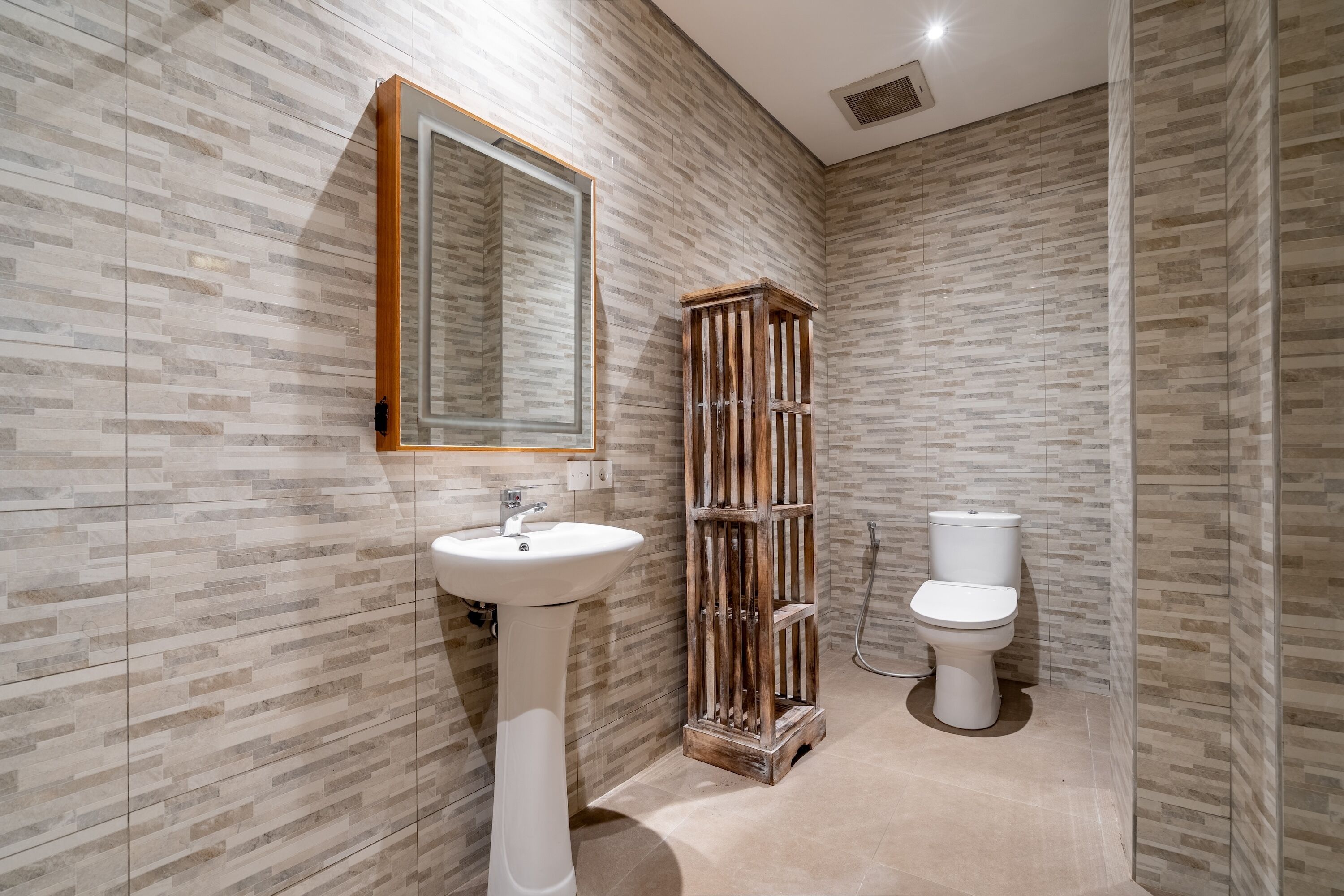 A bathroom with a white pedestal sink, a wooden cabinet, and a toilet.